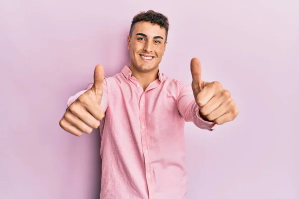 身穿休闲装的西班牙裔年轻人赞成用手做一个积极的手势 微笑着竖起大拇指 为成功感到高兴 优胜手势 — 图库照片