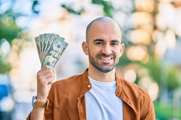 Young hispanic bald man smiling happy holding usa dollars at the city.