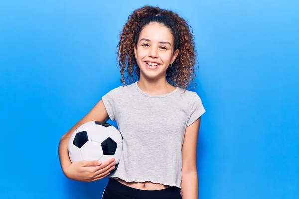 漂亮的小女孩 卷曲的头发 拿着足球 面容积极快乐地站着 微笑着 露出自信的笑容 露出牙齿 — 图库照片