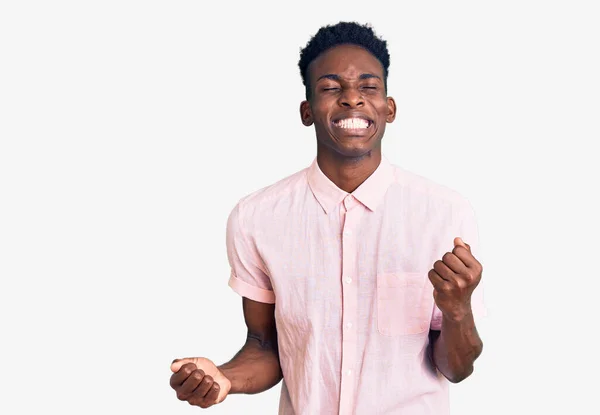 若いアフリカ系アメリカ人の男性は カジュアルな服を着て非常に満足し 腕を上げて勝者のジェスチャーを行う興奮し 笑顔と成功のために叫んでいる お祝いのコンセプト — ストック写真