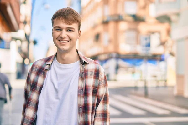 Genç beyaz adam gülümseyerek şehirde mutlu mesut duruyor..