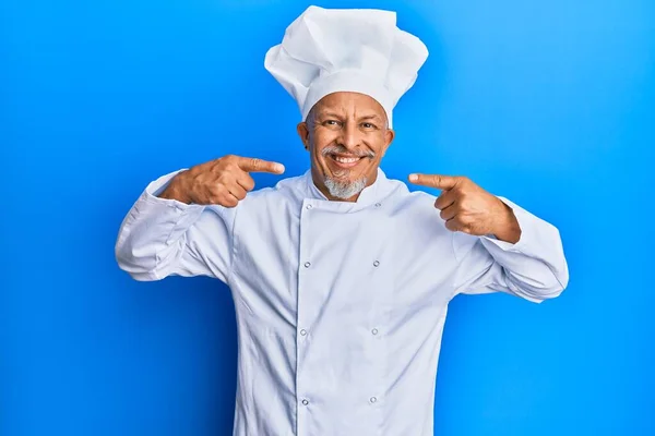 中年白发男子身穿职业厨师制服 头戴帽子 笑容满面 用手指 牙齿和嘴指指点点 牙齿健康概念 — 图库照片