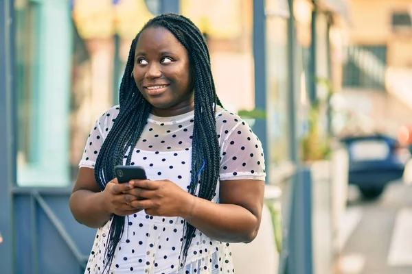 Genç Afrikalı Amerikalı kadın şehirde akıllı telefon kullanarak mutlu bir şekilde gülümsüyor..