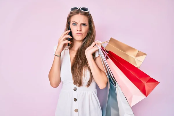 Menina Loira Segurando Sacos Compras Falando Smartphone Cético Nervoso Franzindo — Fotografia de Stock