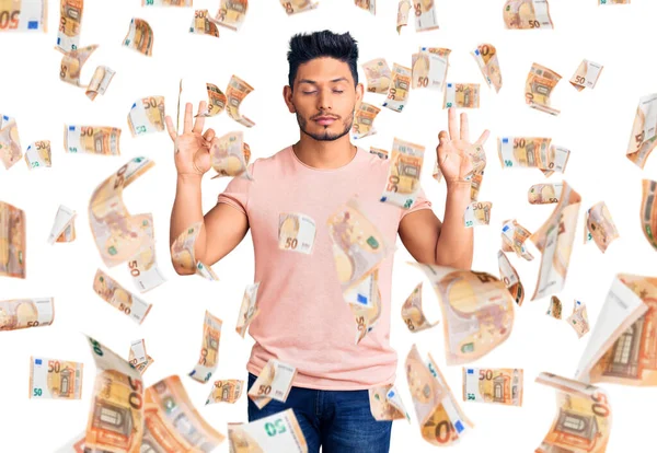 Yakışıklı Latin Amerikalı, günlük kıyafetler giyen rahat ve gözleri kapalı gülümseyen parmaklarıyla meditasyon hareketi yapan genç adam. yoga konsepti.