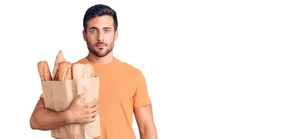 Young Hispanic Man Holding Paper Bag Bread Thinking Attitude Sober — Stock Photo, Image