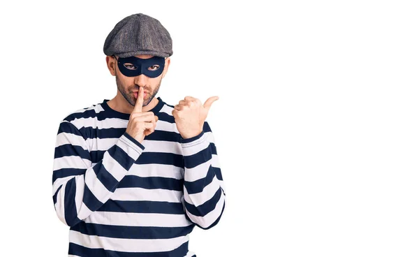 若いハンサムな男が強盗マスクを着用し 唇の側に手を指して指で静かにするように求めている 沈黙と秘密の概念 — ストック写真