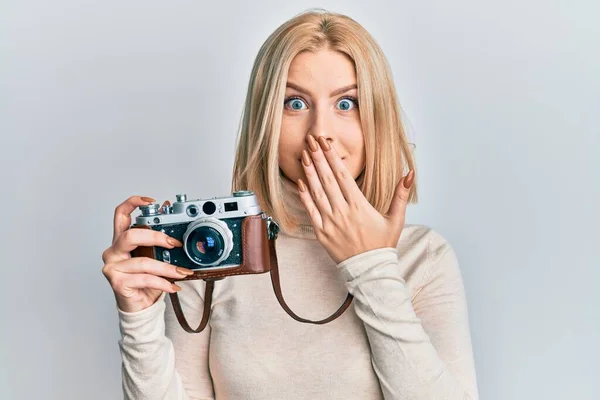 Mladá Blondýnka Držící Zastaralou Kameru Zakrývající Ústa Rukou Šokovaná Vystrašená — Stock fotografie