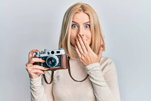 Joven Rubia Sosteniendo Cámara Vintage Cubriendo Boca Con Mano Conmocionada —  Fotos de Stock