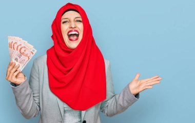 Güzel İspanyol kadın İslami tesettüre bürünmüş elinde Singapur dolarlarıyla zaferi kutlayan banknotlar mutlu bir gülümsemeyle ve ellerini kaldırarak kazanan bir ifadeyle. 