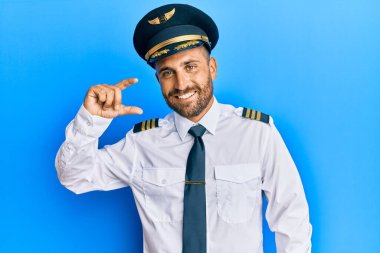 Sakallı, uçak pilotu üniforması giyen, gülümseyen, kendine güvenen, el hareketi yapan, parmaklarıyla işaret yapan ve kameraya bakan yakışıklı bir adam. ölçüm kavramı. 