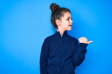 Sevimli İspanyol çocuk, günlük kıyafetler giyiyor, gülümsüyor, gülümsüyor ve başparmağıyla yan tarafa bakıyor.. 