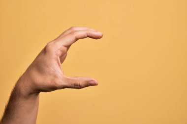İzole edilmiş sarı arka plan üzerinde parmaklarını gösteren beyaz bir adamın eli. Görünmez bir şeyi alıp, parmaklarıyla uzayı gösteren bir nesneyi tutuyor.