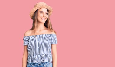 Şapka ve tişört giyen genç ve güzel bir kız yüzünde gülümseme ve doğal bir ifadeyle yan yana bakıyor. Kendinden emin gülen. 