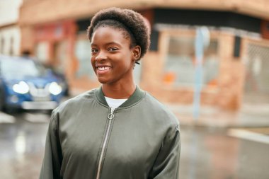 Genç Afrikalı Amerikalı kız gülümseyerek şehirde mutlu mesut duruyor..