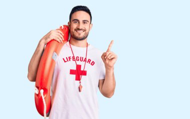 Elinde cankurtaran üniforması tutan genç yakışıklı bir adam bir fikre ya da soru işaretine şaşırmış ve mutlu bir yüzle işaret ediyor. 