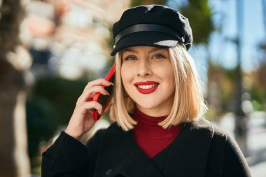Genç sarışın kadın gülümsüyor. Şehirdeki akıllı telefondan konuşuyor..