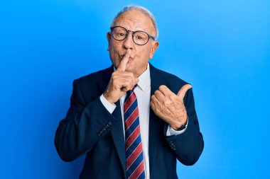 Takım elbiseli, kravatlı, kıdemli beyaz adam sessiz olmak istiyor. Parmakları dudaklarında, elleri yana doğru işaret ediyor. sessizlik ve gizli konsept. 