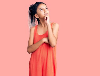 Elleri çenesinde gündelik giysiler giyen tatlı Afro-Amerikan kızı soru sormayı düşünüyor, düşünceli bir ifade. Gülümseyen ve düşünceli bir yüz. şüphe kavramı. 