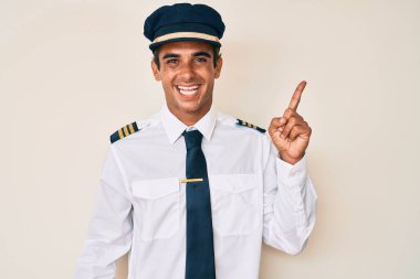 Yüzünde kocaman bir gülümseme olan, uçak pilotu üniforması giyen genç İspanyol adam kameraya el ile işaret ediyor.. 