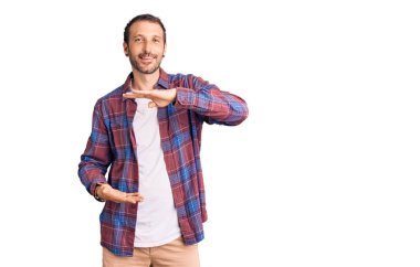 Elleriyle el kol hareketi yapan, büyük ve büyük beden işareti gösteren sıradan kıyafetler giyen genç yakışıklı bir adam. Kameraya bakıp gülümsüyor. ölçüm kavramı. 