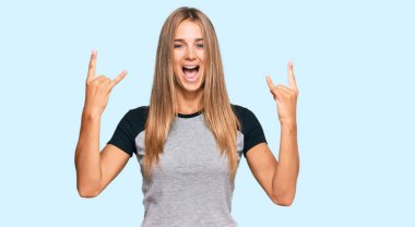 Sıradan kıyafetler giyen, çılgın bir ifadeyle bağıran genç sarışın kadın elleri havada rock sembolü yapıyor. Müzik yıldızı. ağır kavram. 