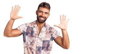 İspanyol asıllı genç adam yaz kıyafetleri giyer ve parmaklarını on numarayla göstererek gülümserken kendinden emin ve mutlu. 