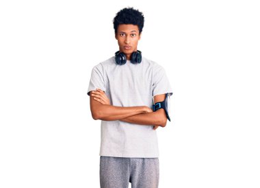 Afrika kökenli Amerikalı genç bir adam spor kıyafetleri giyiyor ve kulaklık takıyor. Kuşkucu ve gergin. Yüzünde çapraz kollarla onaylamayan bir ifade var. negatif kişi. 