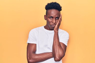 Genç, Afro-Amerikalı bir adam günlük kıyafetler giyip kollarını kavuşturup depresyondan sıkılmış ve yorgun görünüyor.. 