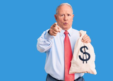 Zarif kıyafetler giyen, elinde para çantası tutan, kamerayı ve seni işaret eden, kendinden emin, ciddi görünümlü, yakışıklı, gri saçlı adam. 