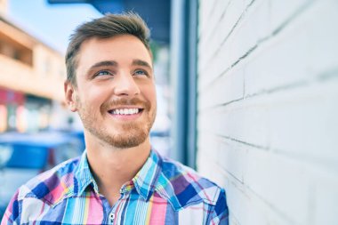 Beyaz bir adam gülümsüyor. Şehrin duvarına yaslanıyor..