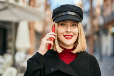 Genç sarışın kadın gülümsüyor. Şehirdeki akıllı telefondan konuşuyor..