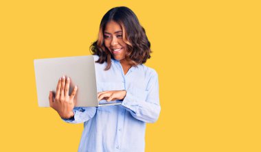 Genç ve güzel melez bir kadın bilgisayarla çalışıyor. Pozitif ve mutlu görünüyor. Kendine güvenen bir gülümsemeyle dişlerini gösteriyor. 