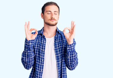 Gündelik kıyafetler giyen yakışıklı beyaz adam rahatla ve parmaklarıyla meditasyon hareketi yaparken gözleri kapalı gülümse. yoga konsepti. 