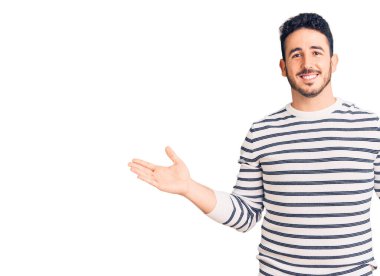 Gündelik kıyafetler giyen genç İspanyol adam gülümseyerek iki elini de açık tutuyor, sunuyor ve reklam karşılaştırması yapıyor ve dengeyi sağlıyor. 