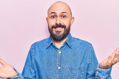 Sıradan kıyafetler giyen, elleri ve kolları havada, kafası karışmış genç ve yakışıklı bir adam. şüphe kavramı. 