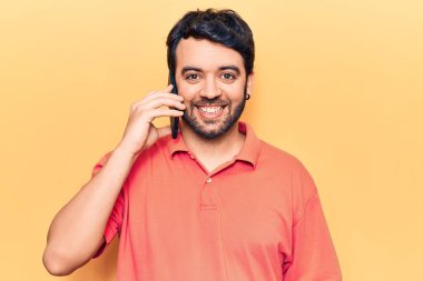 Genç İspanyol adam akıllı telefondan konuşuyor. Olumlu ve mutlu görünüyor. Kendine güvenen bir gülümsemeyle dişlerini gösteriyor. 