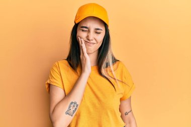 Teslimat üniforması giyen ve diş ağrısı ya da diş hastalığından dolayı ağızlarına acı dolu bir ifadeyle dokunan şapkalı genç İspanyol kadın. dişçi 