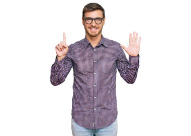 Yakışıklı beyaz adam, günlük kıyafetler ve gözlük takıyor. Altıncı parmaklarını gösterip işaret ediyor. Kendinden emin ve mutlu gülümsüyor.. 