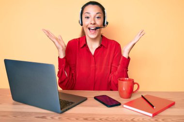 Çağrı merkezinde operatör kulaklığı takan genç esmer kadın zaferi mutlu bir gülümsemeyle ve kazanan ifadeyle kutluyor. 