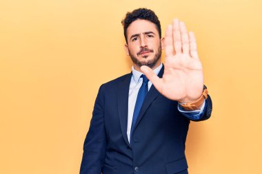 Takım elbiseli genç İspanyol adam avuç içiyle şarkı söylemeyi kesiyor. Yüzünde olumsuz ve ciddi bir jest olan uyarı ifadesi. 