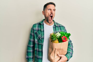 Sakallı yakışıklı bir adam elinde alışveriş torbalarıyla öfkeli ve kızgın çığlıklar atıyor öfkeyle bağırıyor. öfke ve agresif konsept. 