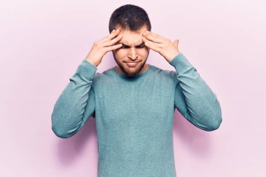 Genç, yakışıklı bir adam, elleri kafasında sıradan bir kazak giyiyor. Stres yüzünden baş ağrısı çekiyor. migren ağrısı. 