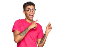 Genç, yakışıklı, Afro-Amerikalı sıradan kıyafetler giyen, gülümseyen ve kameraya bakıp iki elini ve parmağını yana doğru gösteren bir adam.. 