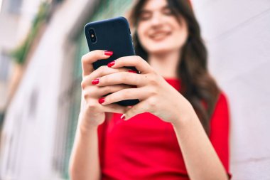 Genç beyaz kadın şehirde akıllı telefon kullanarak mutlu bir şekilde gülümsüyor..