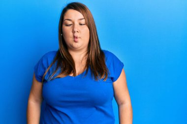 Güzel esmer, iri yarı, günlük mavi tişört giyen dudaklı balık suratlı, çılgın ve komik bir jest yapan bir kadın. Komik ifade. 