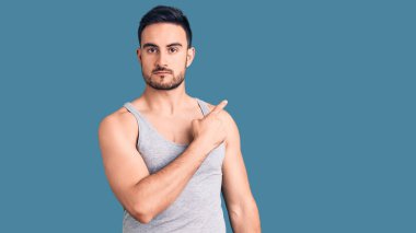 Mayolu ve kolsuz tişörtlü genç yakışıklı bir adam. El parmağı yanda, ciddi ve sakin bir yüz ifadesi sergiliyor. 