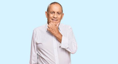 Zarif beyaz tişört giyen yakışıklı. Kameraya kendinden emin bakıyor. Kollarını kavuşturup, çenesini kaldırarak gülümsüyor. Olumlu düşünmek. 