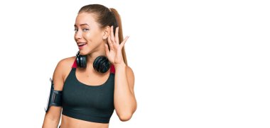 Güzel sarışın kadın spor kıyafetleri giyiyor ve kulaklık takıyor. Kulağından kulağa gülümsüyor. Dedikoduları ve dedikoduları dinliyor. Sağırlık kavramı. 