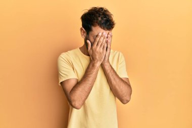 Sarı arka plan üzerine sıradan sarı tişörtler giyen sakallı yakışıklı bir adam. Ağlarken suratını ellerle kapatan üzgün bir ifade. depresyon kavramı. 
